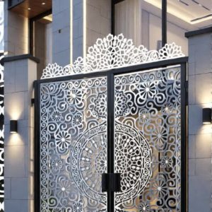 A luxury modern home entrance at night featuring a custom-fabricated, backlit CNC laser-cut black and gold gate. The black central panels are surrounded by intricate gold latticework and a glowing gold 'Sri Yantra' medallion, all topped by an ornate oriental cresting.